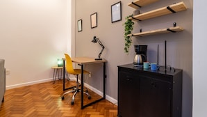 A room with a wooden herringbone floor, a desk with a chair, a black cabinet, and wall-mounted shelves with decorative items.