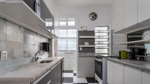 A modern kitchen with white cabinets, a black and white checkered floor, and a window with blinds. - Sea view, 50 metres from the beach | BI701 (Rio de Janeiro)