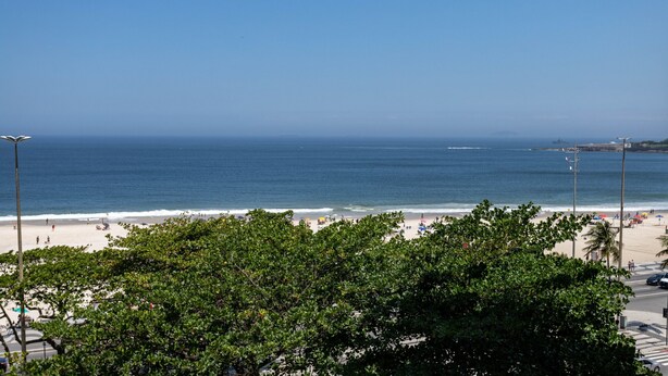 A beach view with a clear sky, trees in the foreground, and a calm sea. - Sea view, 50 metres from the beach | BI701 (Rio de Janeiro)