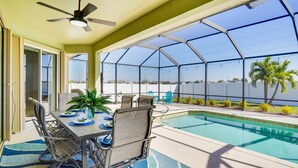 An outdoor pool area with a covered patio, a table with chairs, and a view of the water. - Cozy Cape Coral Home: 8 Mi to Marina! (Cape Coral)