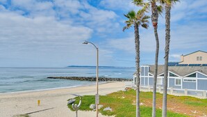 A beach with a street lamp, benches, and palm trees.