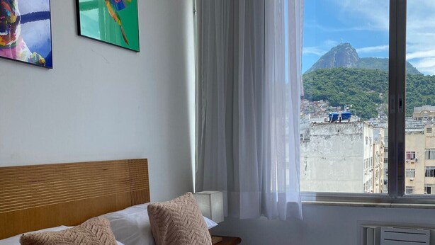 Habitación de hotel con una cama grande, dos almohadas, cabecero de madera y ventana con vistas a la ciudad y una montaña.