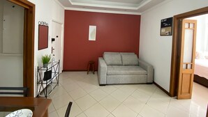 Una habitación con una pared de acento roja, un sofá gris, una mesa de comedor con sillas y una lámpara en el techo.