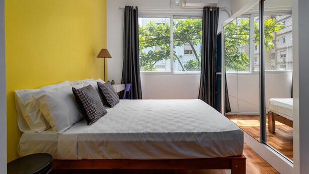A bedroom with a bed, a lamp, a window, and a view of the outside.