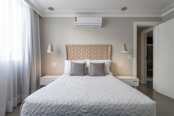Un dormitorio con una cama grande, dos mesitas de noche, un cabecero con diseño geométrico y un equipo de aire acondicionado sobre la cama.