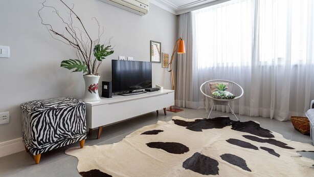 A modern living room with a flat-screen TV, a zebra-patterned ottoman, a cowhide rug, and a large window with sheer curtains. - Modern in Ipanema | Great for families | RE406 Z2 (Rio de Janeiro)
