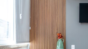 A modern room with a wooden accent wall, a black chair, a small table with a green vase, and a TV mounted on the wall. - Comfort in Copacabana | 150m from the beach | NSC1203 (Rio de Janeiro)