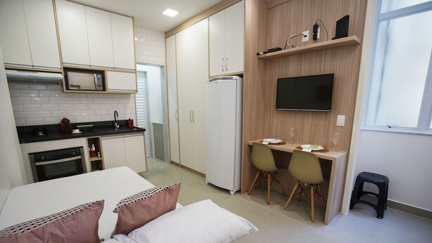 Una cocina compacta con armarios blancos, microondas, refrigerador y un comedor con mesa y sillas.