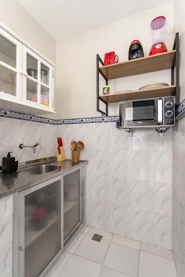 A compact kitchen with a sink, a microwave, and a blender on a shelf.