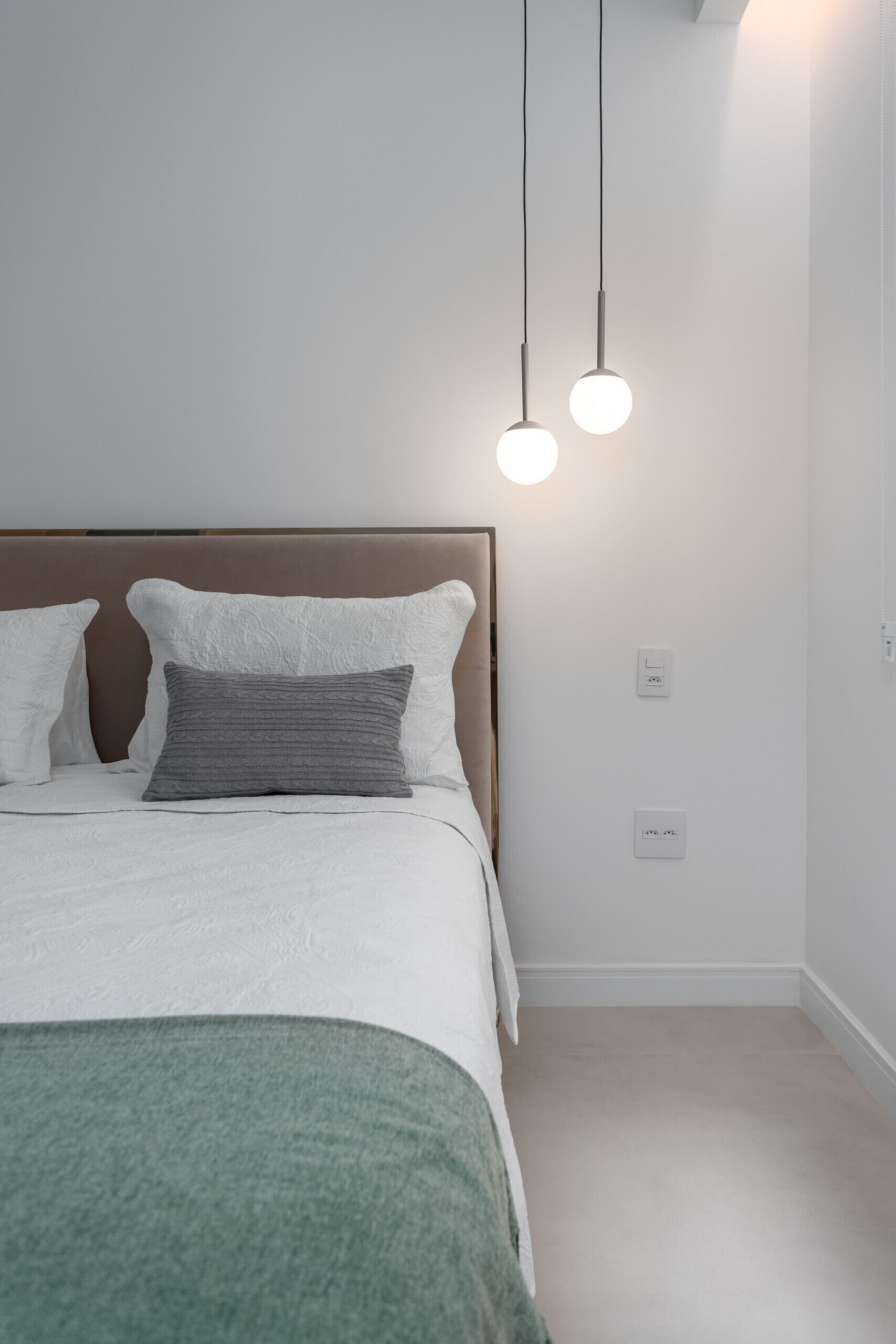 A neatly made bed with a green throw blanket, a wooden headboard, and two bedside lamps.