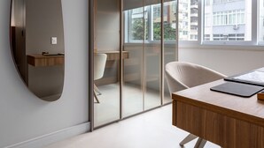 A modern office space with a large desk, a mirror, and a sliding glass door leading to a balcony.