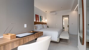 A modern hotel room with a wooden desk, a bed, a bench, and a large mirror.