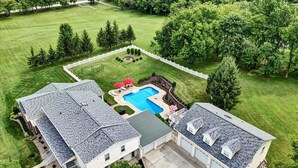 Una casa de dos pisos con un amplio patio trasero, una piscina y un área cercada.