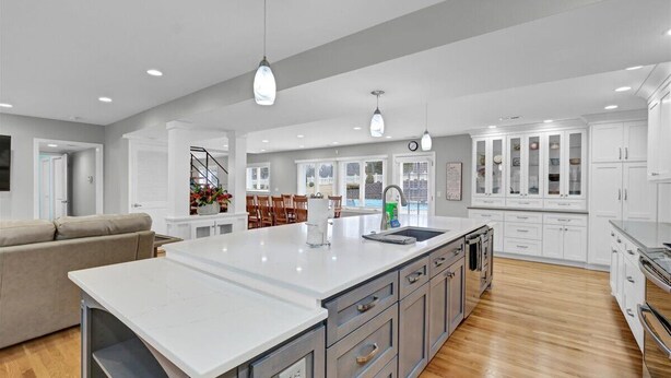 Una cocina amplia con una isla grande, armarios blancos y piso de madera.