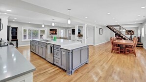 Una cocina amplia con una isla grande, suelo de madera y un comedor con una escalera que sube a otro nivel.