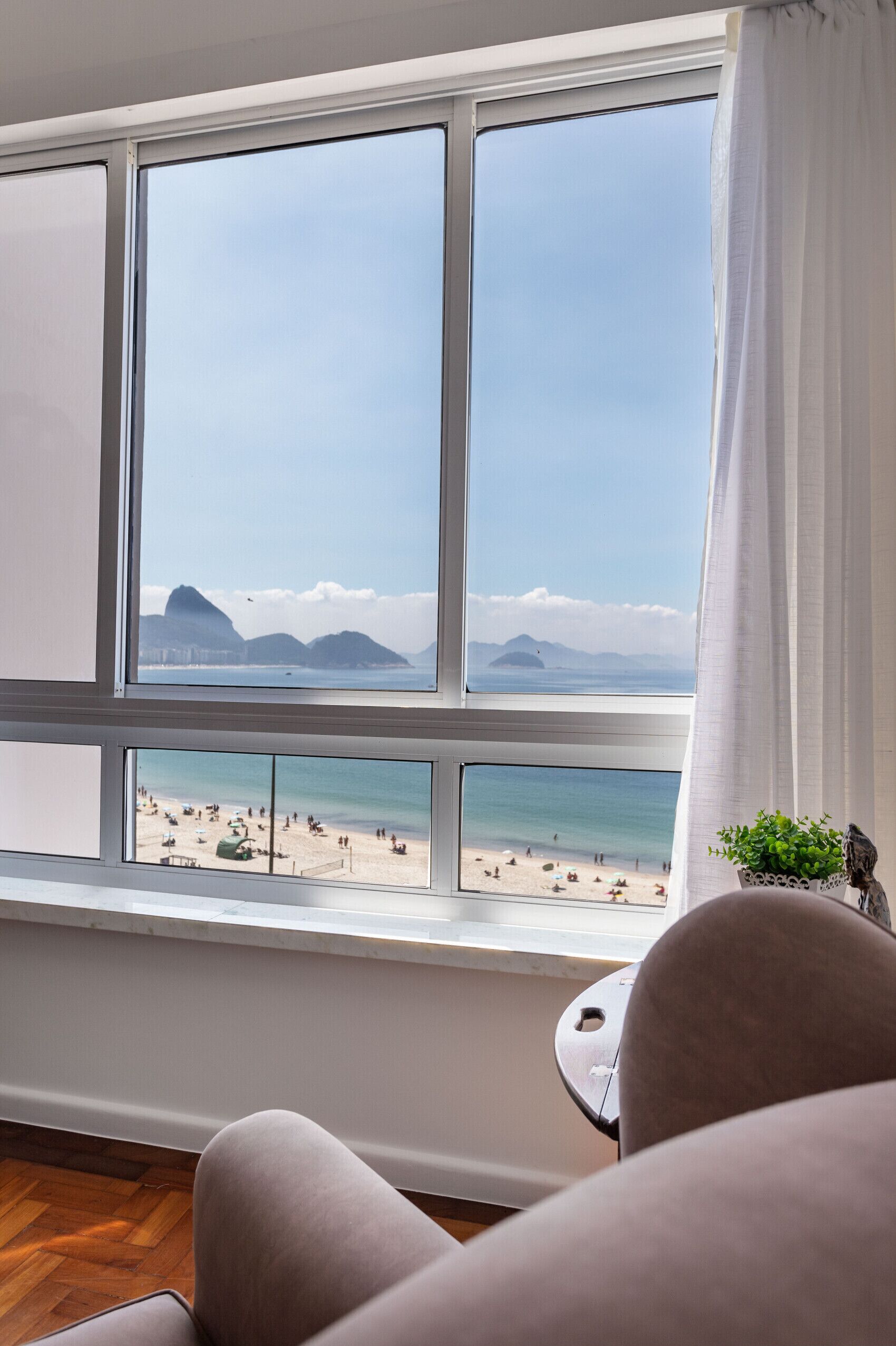 A room with a large window overlooking a beach, a small table, and a chair.