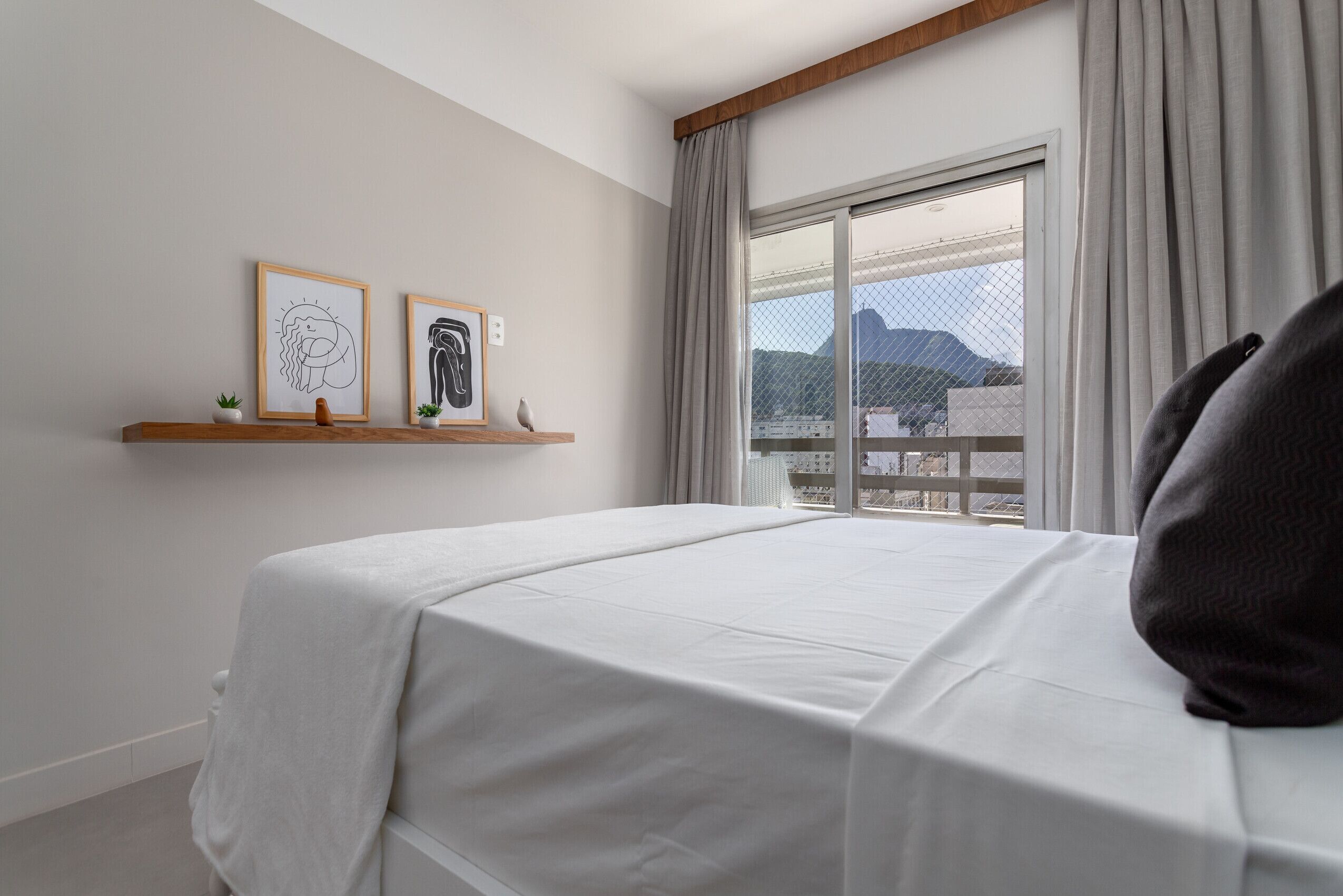 A hotel room with a large bed, a window with a view of mountains, and two framed artworks on the wall.