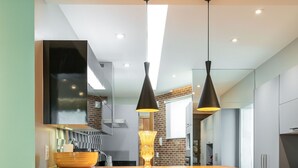 Una cocina moderna con barra de madera, tres taburetes, luces colgantes y un espejo grande sobre el lavamanos.
