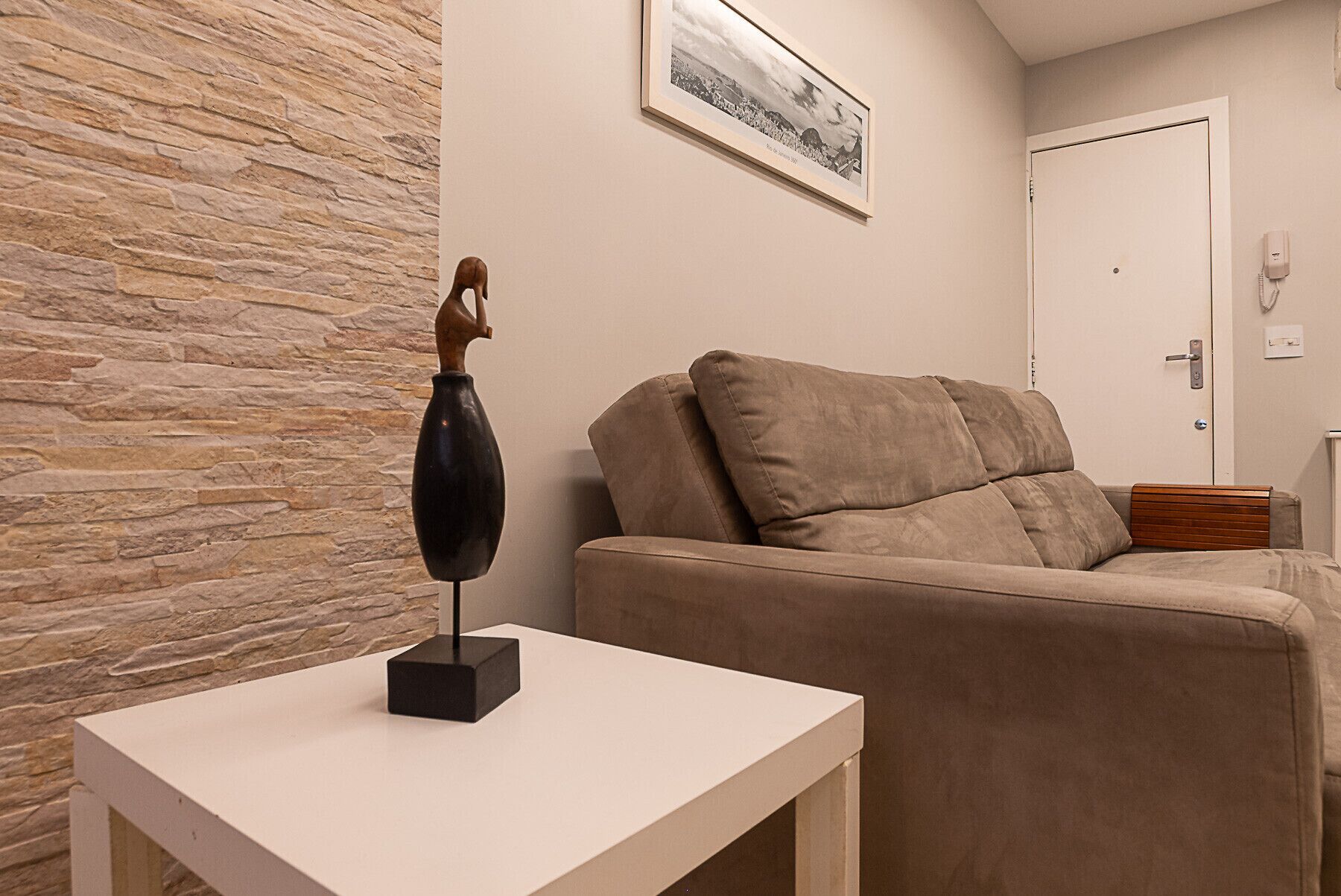 En stue med en stenvæg, en beige sofa, et hvidt bord og et billede i ramme på væggen.