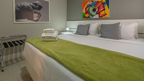 A hotel room with a bed, pillows, a green blanket, a chair, a nightstand with a lamp, and artwork on the walls. - 3 minutes from Copacabana beach | STC303 (Rio de Janeiro)