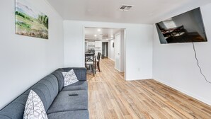 Ein modernes Wohnzimmer mit grauem Sofa, einem wandmontierten Flachbildfernseher und Holzboden.