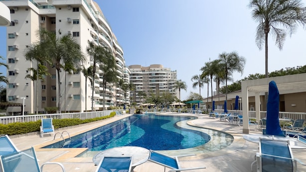 A swimming pool with lounge chairs and palm trees, surrounded by multi-story buildings. - Beauty at Recreio | For 5 peopple | SA201 (Rio de Janeiro)