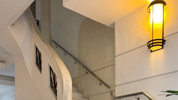 Un escalier en marbre avec une rampe, un luminaire fixé au mur et un meuble noir adossé au mur.