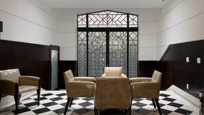 Une pièce dotée d’un sol à carreaux, d’un espace salon central avec quatre chaises et d’une cloison décorative ornée de motifs géométriques.