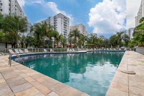Une piscine entourée d’immeubles imposants, avec des chaises longues et des palmiers.