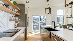 A modern kitchen with a built-in stove, wooden shelves, and a large window overlooking a balcony. - Hot Tub & Panoramic Mtn Views: Pine Retreat! (Pine)