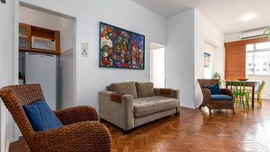 A living room with a sofa, wicker chairs, a dining table, and a large abstract painting.