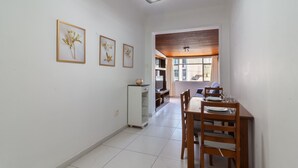 A dining area with a wooden table and chairs, a refrigerator, and framed floral artwork on the wall.