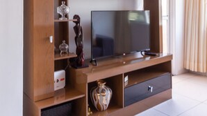 A modern living room with a large flat-screen TV on a wooden entertainment unit, a vase, and a decorative sculpture.