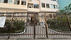 A multi-story residential building with a gated entrance, a tiled patio area, and surrounding greenery.