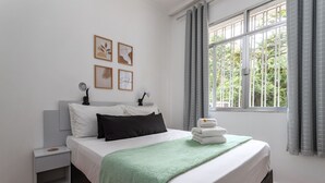 A neatly made bed with a green blanket, white bedding, and a small nightstand with a lamp.