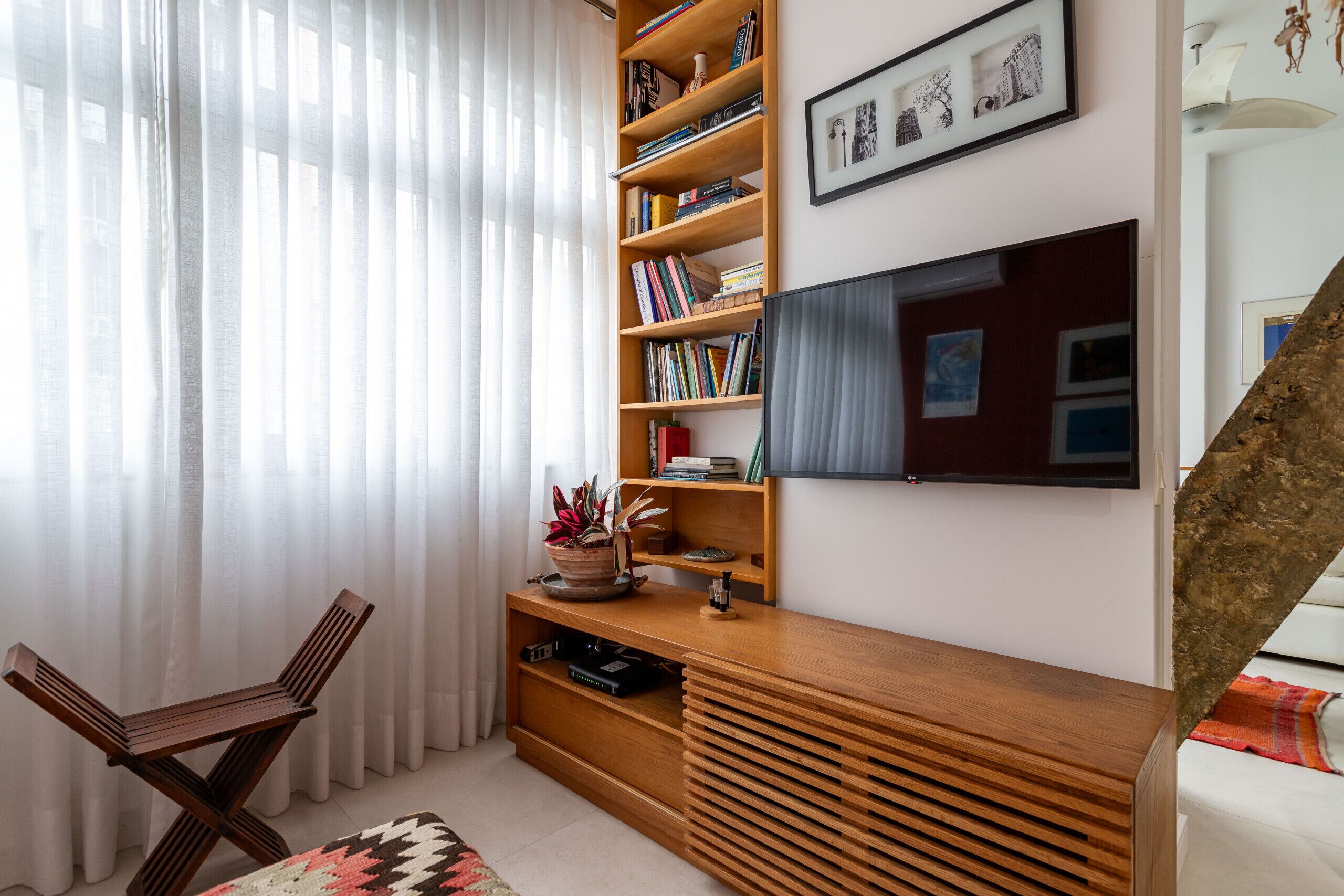 Un salon moderne avec une bibliothèque en bois, un téléviseur à écran plat fixé au mur et un coin salon confortable agrémenté d’un tapis à motifs.