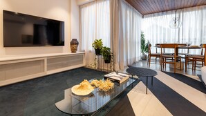 Una sala de estar moderna con televisor de pantalla plana, una mesa de centro de vidrio y un comedor con mobiliario de madera.