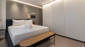 Una habitación de hotel moderna con una cama grande, un banco, una mesita de noche y un armario.