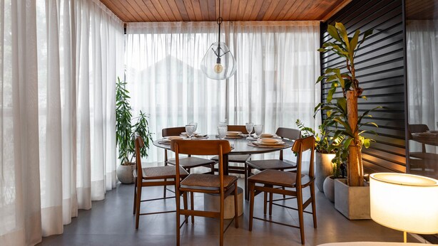 Un comedor con una mesa redonda, sillas de madera y plantas en macetas.