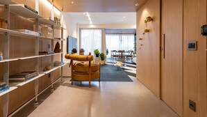 Un interior moderno con estanterías de madera, una zona de estar central y una mesa de comedor al fondo.