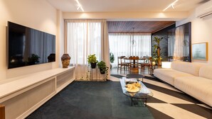 Una sala de estar moderna con un televisor de pantalla plana grande, un sofá, una mesa de centro y una zona de comedor con sillas y una mesa.