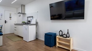 A modern kitchen with white cabinets, a built-in oven, and a stainless steel range hood. A flat-screen TV is mounted on the wall above the counter. - Friendly in Copa | Ideal for couples | NSC1209 (Rio de Janeiro)