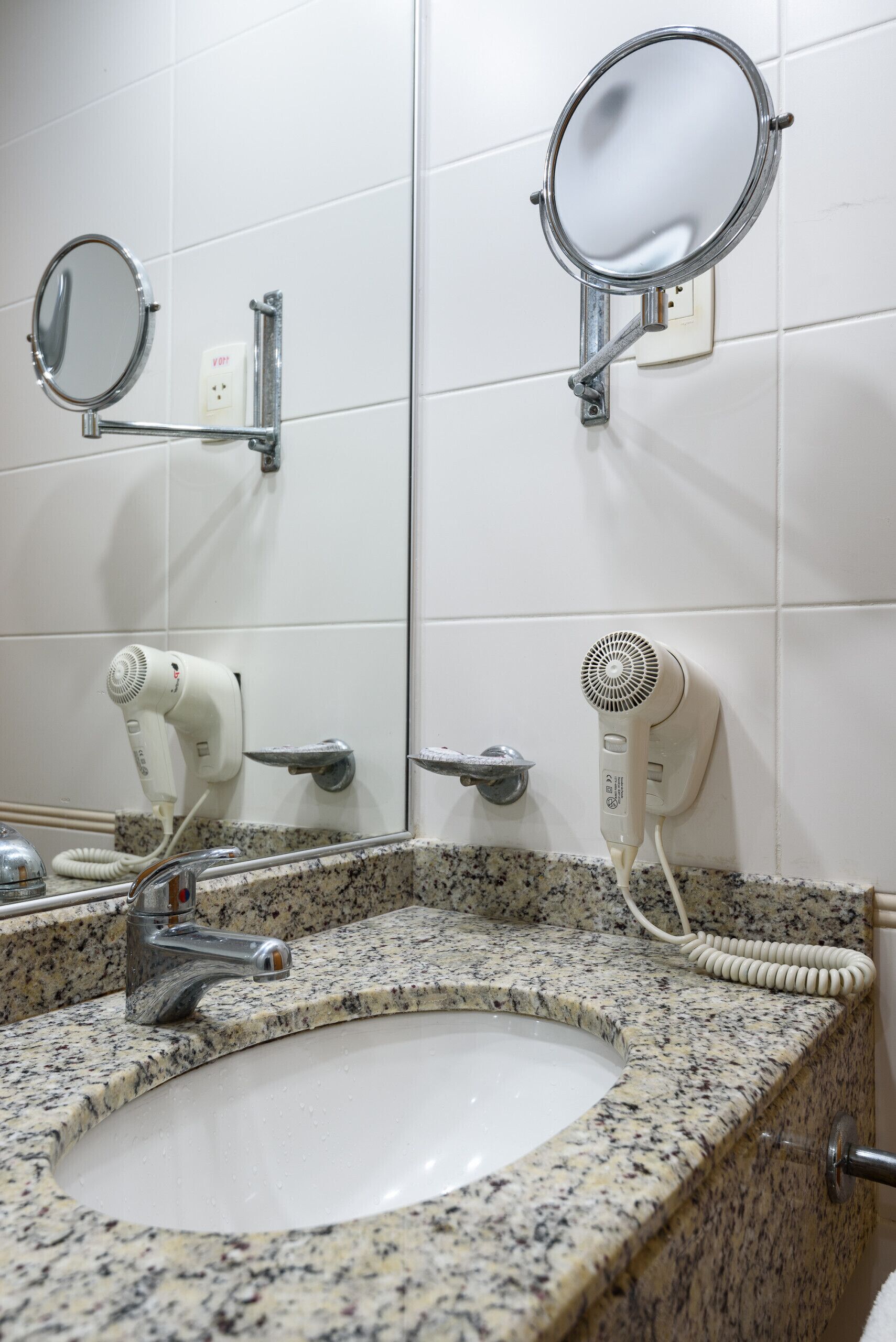 A bathroom with a granite countertop sink, a mirror, and two hair dryers mounted on the wall.