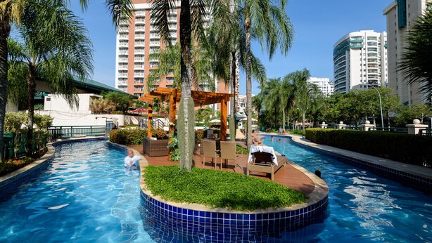 A swimming pool with a circular island, palm trees, and outdoor seating. - Suite, pool and gym | BPremium T4 Z10 (Rio de Janeiro)