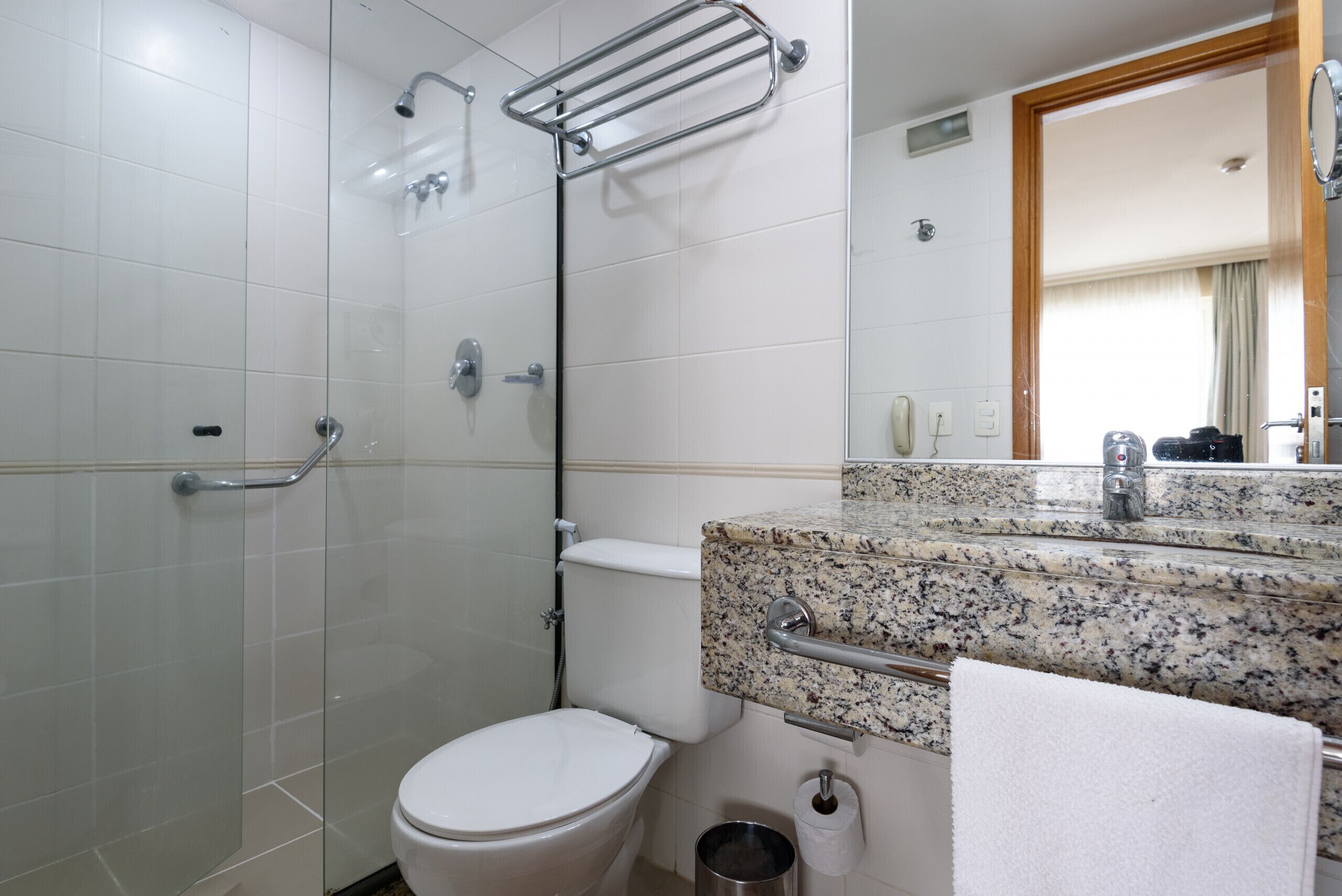 Ein Badezimmer mit Duschkabine aus Glas, einer weißen Toilette, einer Arbeitsplatte aus Granit und einem Spiegel.