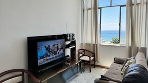 Ett vardagsrum med en tv, en soffa, en fåtölj och ett fönster med utsikt över havet.