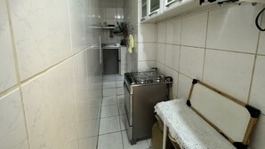 Ett kompakt kök med vita kakelplattor, en spis, ett handfat och en mikrovågsugn.