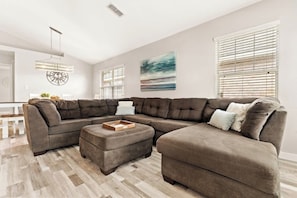A modern living room with a sectional sofa, ottoman, and a pendant light.