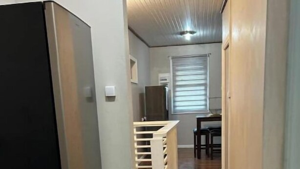A narrow hallway with a refrigerator on the left, a wooden cabinet in the center, and a dining area with a table and chairs at the end. - Modern and Centrally located. (Forte de France)