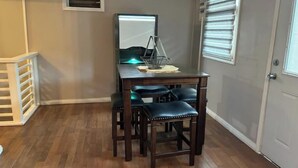 A room with a wooden desk, two chairs, a small table with a lamp, and a window with blinds. - Modern and Centrally located. (Forte de France)